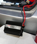 Score This Badass 1000 Watt DC To AC Power Inverter displaying compact design with input cables in a vehicle trunk.