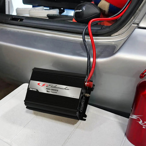Score This Badass 1000 Watt DC To AC Power Inverter displaying compact design with input cables in a vehicle trunk.