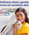 Woman smiling, holding soft blanket with Unscented Dryer Sheets 240 Count For Sensitive Skin Hypoallergenic Dermatologist Tested in background.