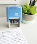 No Mess Self Inking Custom Stamp Kit With Dual Shade Blue And Red Ink Pads, on a desk with an invoice and green plant.