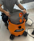 Person inserting Reusable Dust Bag For Ridgid And Craftsman Shop Vacuums into an orange vacuum, showing its fit and ease of use.