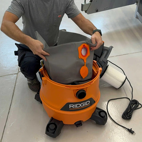 Person inserting Reusable Dust Bag For Ridgid And Craftsman Shop Vacuums into an orange vacuum, showing its fit and ease of use.