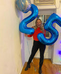 Person holding deep navy blue 25 balloon set, used as party decor and photo booth prop for birthday backdrop celebration.