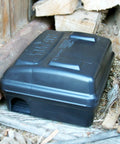 Titan Rodent Bait Station For Commercial Pest Control Weighted Self Securing Design installed outdoors near wooden planks