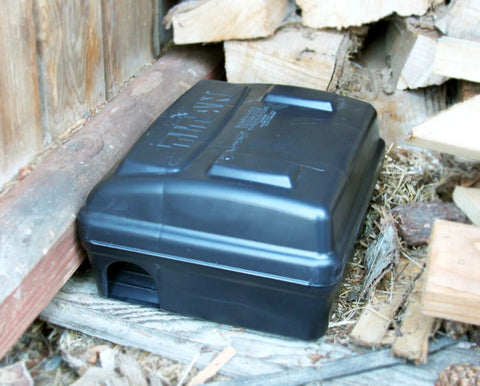 Titan Rodent Bait Station For Commercial Pest Control Weighted Self Securing Design installed outdoors near wooden planks