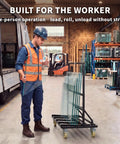 Heavy Duty Folding Drywall Cart Dolly With 1800 Lbs Capacity For Panels Plywood Lumber And Glass, Adjustable Handle Height For Easy Push On The Job, Steel Frame Black, A Real Workhorse For On Site Construction And Warehouse. Worker loading glass panels on black steel cart in warehouse