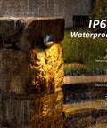 Low Voltage LED Deck Lights 12-24V 6 Pack illuminating a stone pillar in rain, showcasing IP65 waterproof and warm 3000K glow