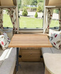 Heavy Duty Aluminum RV Table Leg Equipped With 360 Swivel And Adjustable Height Plus Space Saving Bracket For Camper Motorhome Yacht Setup Rock Solid Base Black positioned under a wooden table in a cozy RV setting.