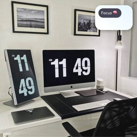 Modern home office desk setup with dual screens, black desk mat, and decorative artwork.
