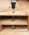 PINOZE 14-piece spade drill bit set; teal cordless drill drilling a hole in plywood on a workbench