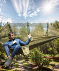 Man relaxing in Go-To Portable Camping Hammock With Mosquito Net for Outdoor Adventures, green tent in a forest setting.