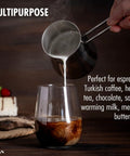 Pouring milk from Go-To Turkish Coffee Pot Cezve Ibrik Briki Stainless Steel Stove Top Pot into a glass, with cake in the background.