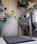 Industrial workspace with machinery, fan overhead, and caution signs on walls.
