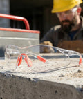 Straight Up Durable Four Pack Kickass Wraparound Safety Glasses Featuring Soft Silicone Frames And Ansi Z871 Certified Lenses For Slick Everyday Eye Protection That Hits Just Right on a worksite with a blurred worker in the background.