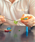 Person using Clear All Purpose Glue In Four 3 Gram Tubes With Fast Setting for Projects and Repairs on a craft project with colored beads.