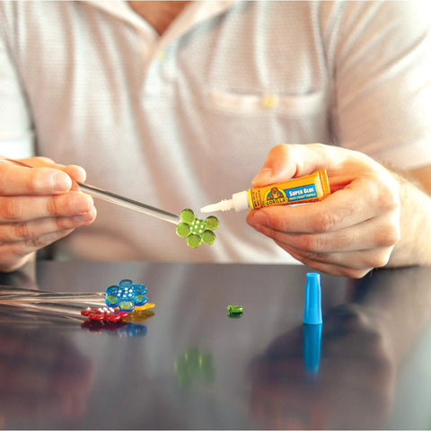 Person using Clear All Purpose Glue In Four 3 Gram Tubes With Fast Setting for Projects and Repairs on a craft project with colored beads.