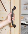 Hand gripping Ten Inch Barn Door Pull Handle Set, Rustic Black Solid Steel With Powder Coat Finish, installed on a wooden door