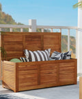 Acacia Wood Deck Box 46 Gallon Outdoor Storage Bin For Patio Cushions Pillows Garden Tools Pool Accessories And Wooden Porch Bench Indoor Outdoor Storage Chest on a deck with colorful cushions inside.
