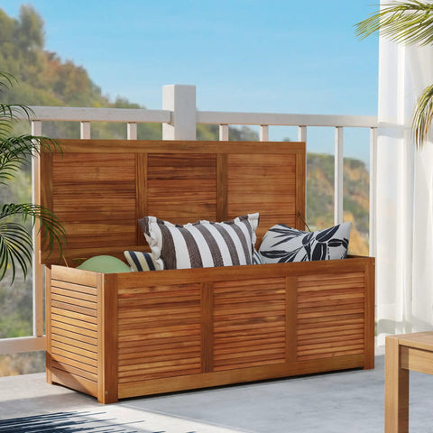 Acacia Wood Deck Box 46 Gallon Outdoor Storage Bin For Patio Cushions Pillows Garden Tools Pool Accessories And Wooden Porch Bench Indoor Outdoor Storage Chest on a deck with colorful cushions inside.