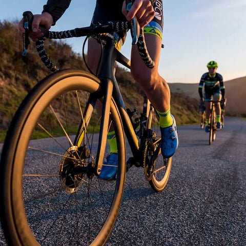 Cyclists riding on a road with a focus on bike wheels showcasing heavy duty bike quick release axle skewer set for front and rear hollow shaft kit replacement on road mountain MTB BMX bikes steel 1045 axles with aluminum quick release fits 20 to 28 inch wheels 6 to 8 speed.