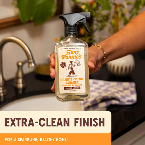 Person holding Granite And Stone Daily Countertop Cleaner With Plant Based Formula in front of kitchen sink.