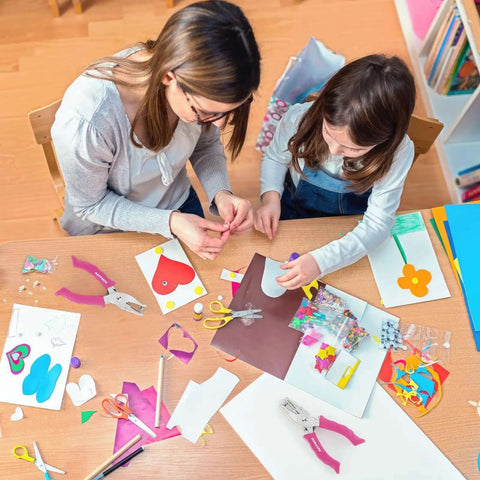 Two people crafting with the One Hole Punch With Soft Grip Handle For Paper One Quarter Inch Hole Punch Pink, surrounded by colorful paper.