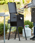 Front view: Propane grill on a metal stand with lid open; black finish, thermometer on front, propane tank nearby.
