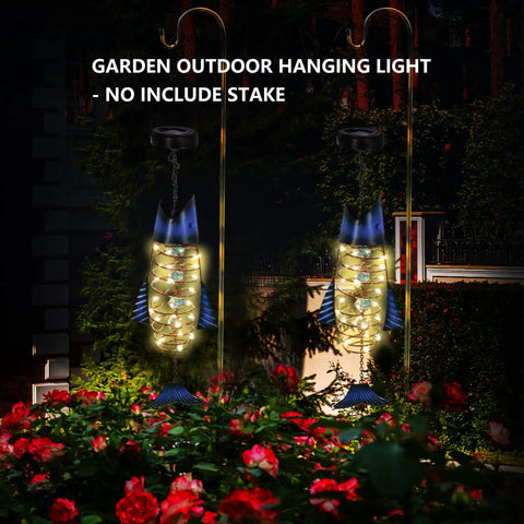 Handcrafted Iron Fish Lantern With Solar Powered Warm White LED Lights hanging in a garden at night, IP65 waterproof.