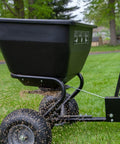 Tow Behind Broadcast Spreader With Universal Hitch 175 Lb Capacity Durable Poly Hopper spreading seeds on lawn