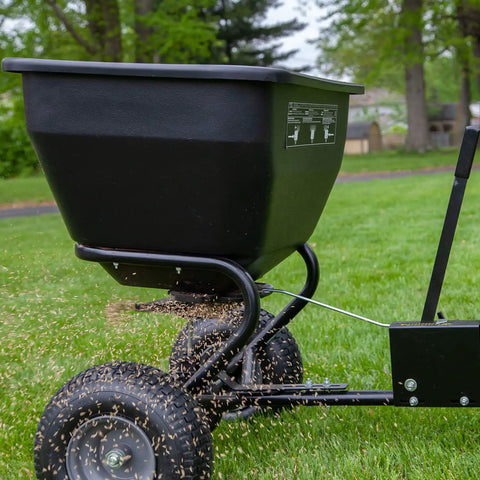 Tow Behind Broadcast Spreader With Universal Hitch 175 Lb Capacity Durable Poly Hopper spreading seeds on lawn