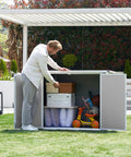 Man organizing items in a spacious outdoor storage shed with floor included, 41 cu ft resin weatherproof storage box, grey and white.