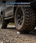 Badass 80Gbps M.2 Nvme Ssd Enclosure under a vehicle tire for extreme data protection and crush resistance on rough terrain.