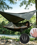 Person relaxing in an All In One Camping Hammock With Mosquito Net And Rain Fly Tarp over a river. Features ultra-fine mesh screen.