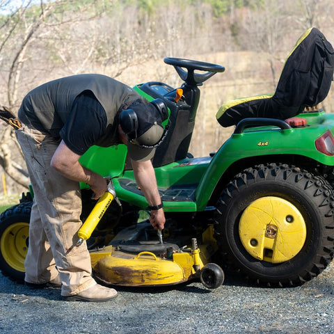 Side view of a yellow LockNLube premium pistol-grip grease gun used on a green riding mower