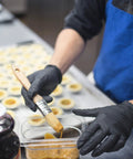 AMMEX X3 black nitrile disposable gloves, close-up of gloved hands glazing pastries in a kitchen