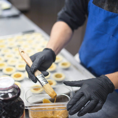 AMMEX X3 black nitrile disposable gloves, close-up of gloved hands glazing pastries in a kitchen