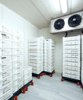 Industrial storage room with white plastic crates stacked on mobile carts with red wheels.