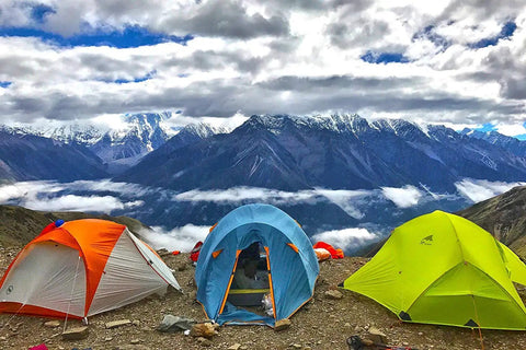 Tents in vibrant colors on a mountain landscape with clouds and peaks in the background.