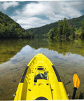 Yellow kayak on calm lake with paddles, surrounded by forest and hills under blue sky with clouds.