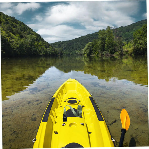 Yellow kayak on calm lake with paddles, surrounded by forest and hills under blue sky with clouds.
