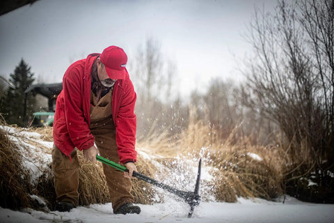 Man using Heavy Duty Pick Mattock With Forged Steel Head And Solid Fiberglass Core, Ergonomic No Slip H Grip Handle in snowy field