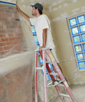 Man using Cling Cover Plastic Sheeting 9 Ft By 400 Ft Dispenser Box That Grips Surfaces Without Tape for painting prep on a brick wall.