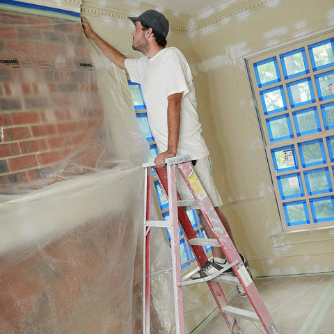 Man using Cling Cover Plastic Sheeting 9 Ft By 400 Ft Dispenser Box That Grips Surfaces Without Tape for painting prep on a brick wall.