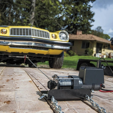 2000 Lb 12V Electric Winch With Steel Cable, Hook And Corded Remote on wooden platform pulling a yellow car