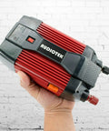 Heavy Duty 900W Peak Power Inverter Converts Dc 12V To Ac 110V held in hand against a white brick wall.