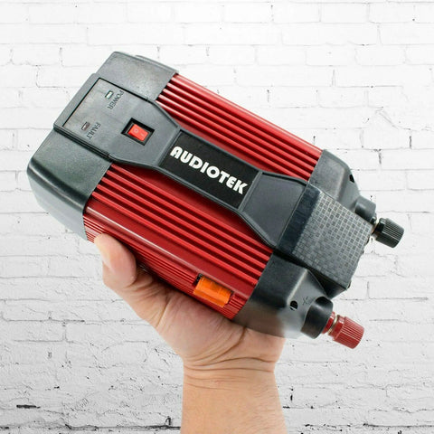 Heavy Duty 900W Peak Power Inverter Converts Dc 12V To Ac 110V held in hand against a white brick wall.