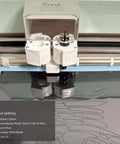 Front view of Cricut cutting machine head cutting 12x12 in opaque black PET stencil sheet