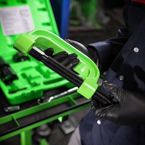 Close-up of a mechanic holding a green C-frame from a 21 Piece Ball Joint Press Kit With Puller And U Joint Adapters For Upper And Lower Ball Joints Brake Pins And More Pro Grade Automotive Tool Set For 2 Wheel Drive And Four Wheel Drive Vehicles