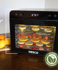 Top Shelf Eight Tray Stainless Steel Food Dehydrator Running Smooth With Digital Timer And Adjustable Temp Control Made For Killer Jerky Dried Fruits Veggies Fresh Herbs Dog Biscuits 650W Bpa Free showing oranges and herbs on trays.