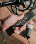 Close-up of a hand holding a 16 notch bottom bracket tool, engraved with 'BIKE HAND YC-306BB', on a wooden surface.